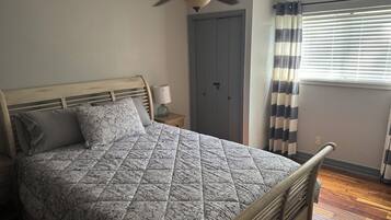 Een slaapkamer met een bed, een plafondventilator, een nachtkastje, een deur en een raam met jaloezieën.