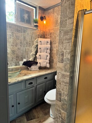 A bathroom with a stone wall, a sink with a glass bowl, and a toilet. - Charming Waterwood Getaway 2BR/2BA Golf Retreat Near Lake Livingston (Huntsville)