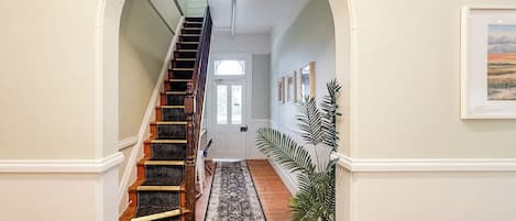 A hallway with a wooden staircase, a patterned rug, and a potted plant.