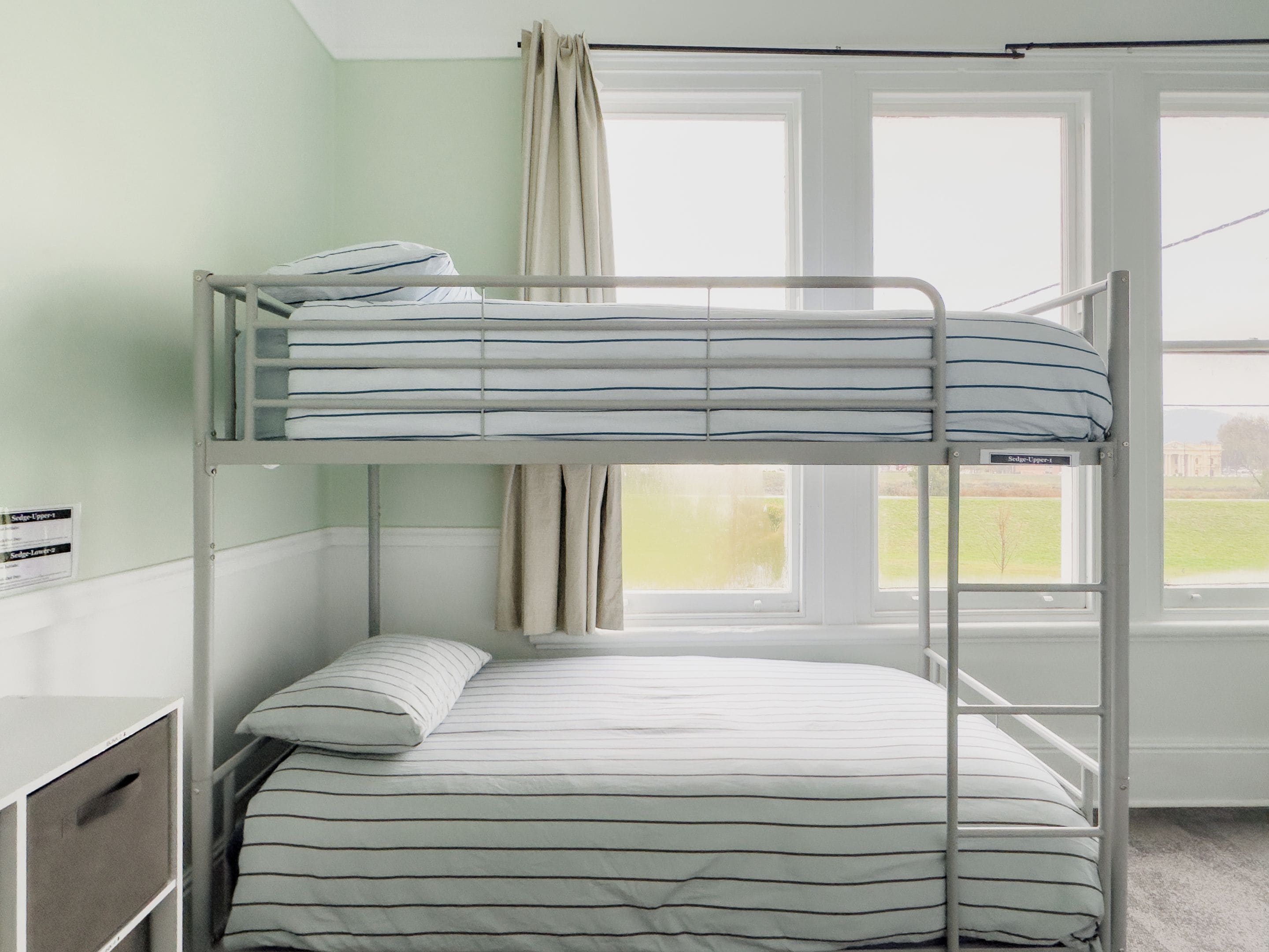 A bunk bed with striped bedding, a window with curtains, and a view of a building outside.
