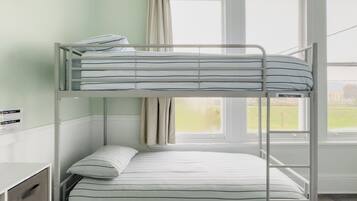 A bunk bed with striped bedding, a window with curtains, and a view of a building outside.