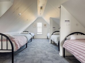 Quarto em dormitório com duas camas de solteiro, uma janela e um ventilador de teto.