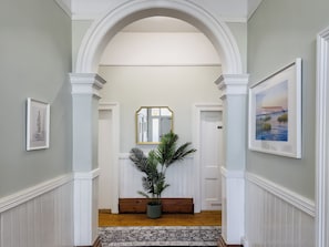 Un pasillo con un arco blanco, una planta en maceta, un espejo y cuadros en las paredes.