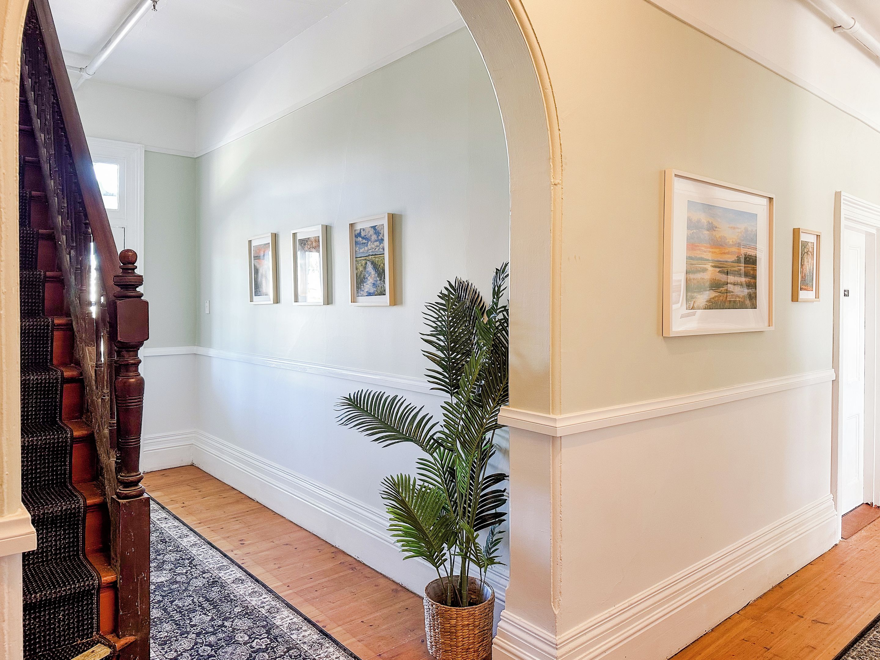 A hallway with a wooden staircase, a patterned rug, and framed artwork on the walls.
