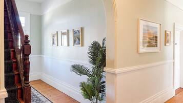 A hallway with a wooden staircase, a patterned rug, and framed artwork on the walls.