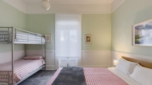 A room with bunk beds, a large bed, a checkered bedspread, a black rug, a white door, and a framed picture on the wall. - The Fenway Hostel (Invermay)
