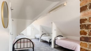 A dormitory room with three bunk beds, a brick wall, and a ceiling light fixture. - The Fenway Hostel (Invermay)