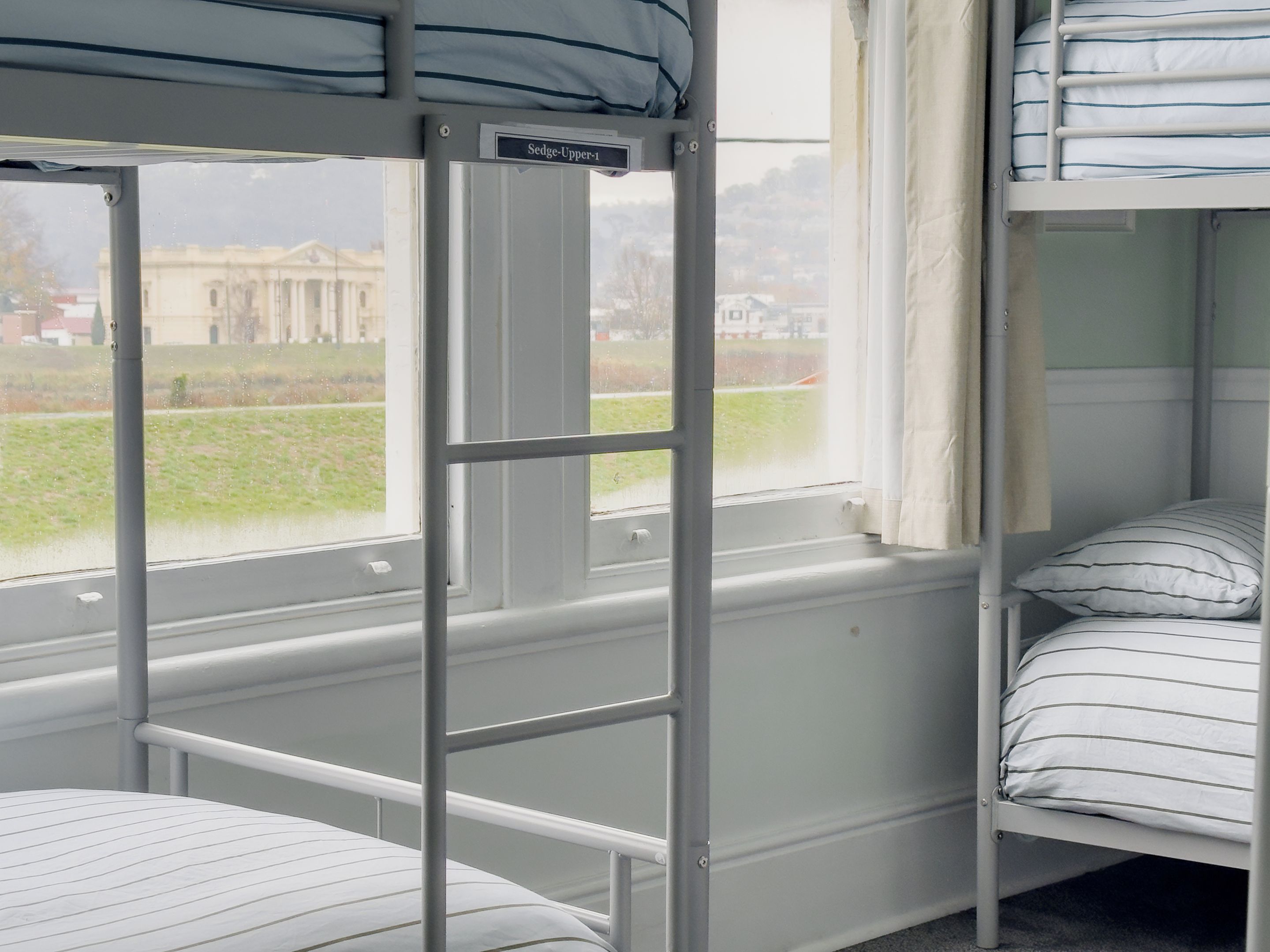 A bunk bed room with a window, a metal ladder, and a sign indicating 'Sedge-Upper-1'.