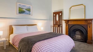 A bedroom with a bed, a painting, a mirror, and a fireplace. - The Fenway Hostel (Invermay)