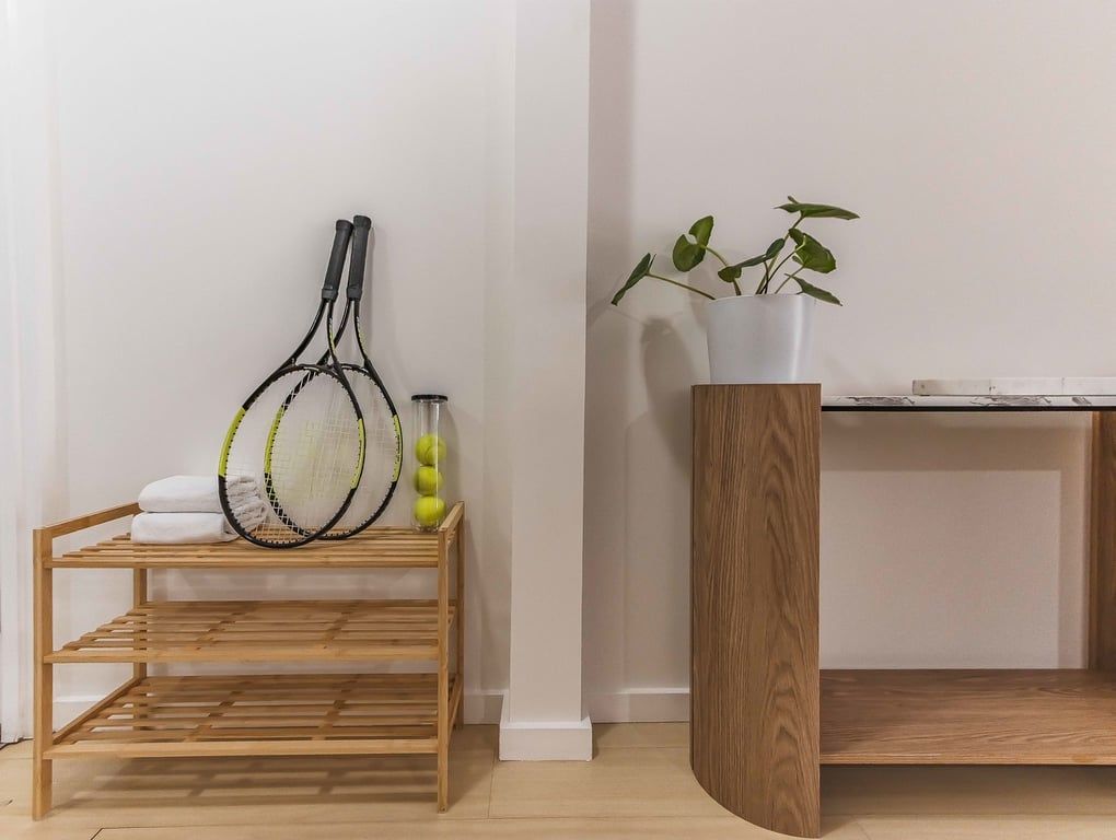 A wooden rack with tennis rackets and a potted plant on a white wall.