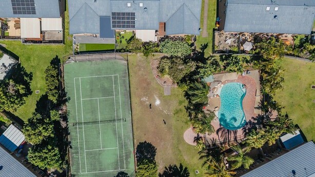 Eine Luftaufnahme eines Wohngebiets mit Tennisplatz, Schwimmbad und mehreren Häusern mit geneigten Dächern.