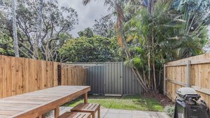 Eine Holzterrasse mit Picknicktisch und Bänken, umgeben von einem Holenzaun und üppigem Grün.