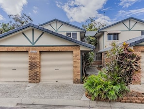 A residential property with two garage doors, a brick chimney, and a landscaped garden with various plants. - Sunkissed at Kirra (Tweed heads)