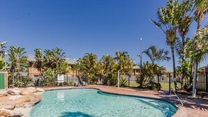 Ein Swimmingpool mit Pflasterung, umgeben von Palmen und einem Zaun.