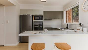 A modern kitchen with a central island, bar stools, and a clock on the wall.