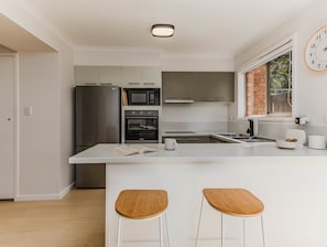 A modern kitchen with a central island, bar stools, and a clock on the wall. - Sunkissed at Kirra (Tweed heads)