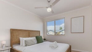Ein Schlafzimmer mit einem hölzernen Bett, einem Nachttisch, einem Deckenventilator, einem Fenster mit Blick und einem gerahmten Bild an der Wand.