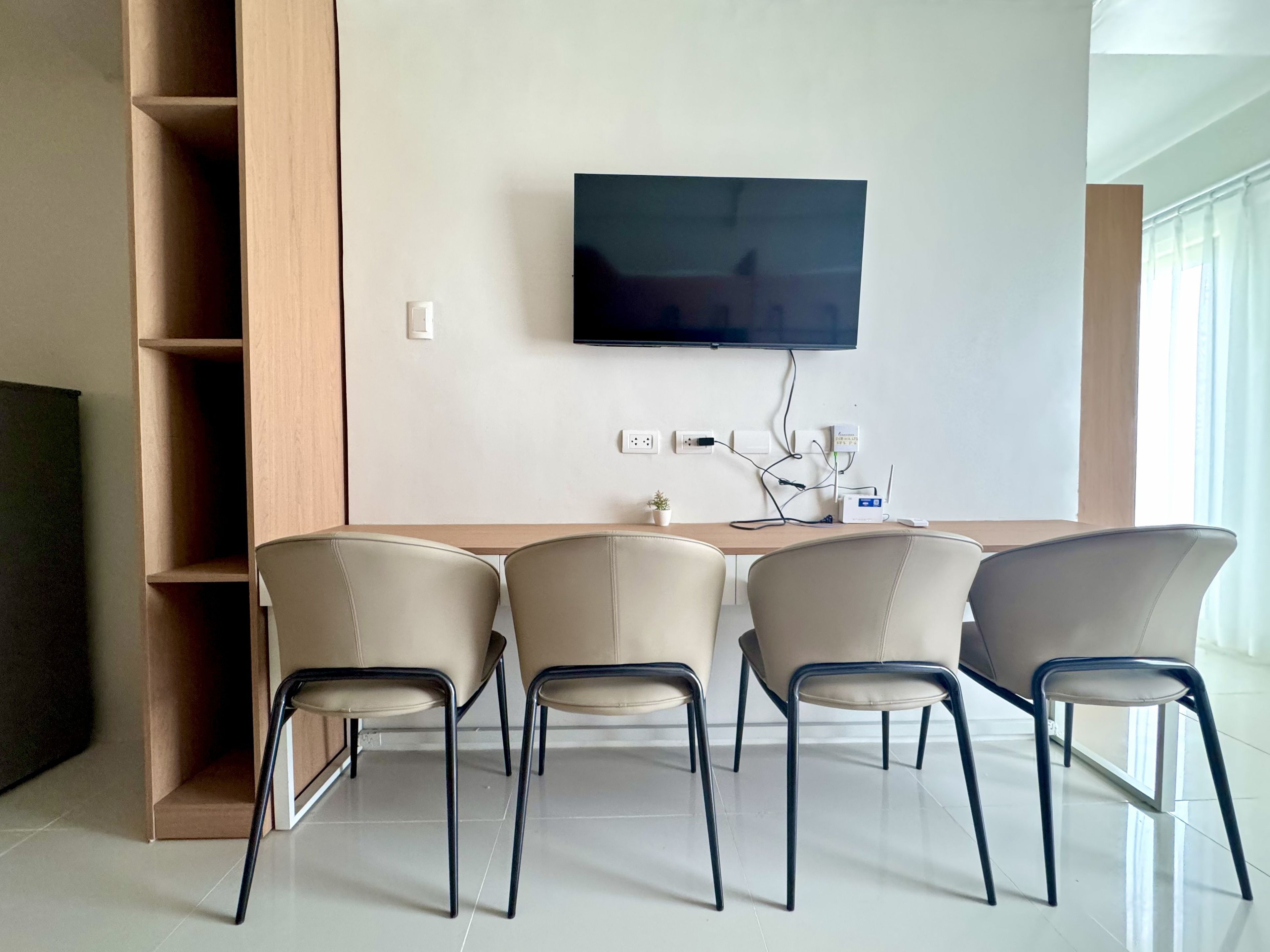 A modern living room with a flat-screen TV mounted on the wall, a wooden sideboard, and four chairs with metal legs.
