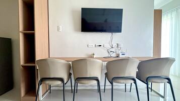 A modern living room with a flat-screen TV mounted on the wall, a wooden sideboard, and four chairs with metal legs.