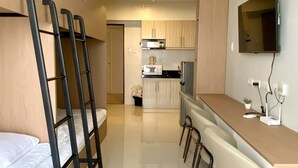 A compact room with bunk beds, a kitchenette, a dining area, and a TV mounted on the wall. - Royal Oceancrest Panglao 1 (Dauis)