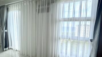 A room with a large window covered by sheer white curtains, a tiled floor, and a visible cityscape view.