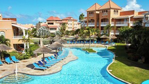 A resort with a swimming pool, lounge chairs, and palm trees. - 2-bedroom Penthouse Condo in Divi Golf & Beach with breathtaking Oceanfront view (Oranjestad)