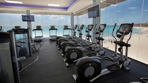 A gym with cardio machines and weights, large windows with a beach view, and a modern ceiling design. - 2-bedroom Penthouse Condo in Divi Golf & Beach with breathtaking Oceanfront view (Oranjestad)