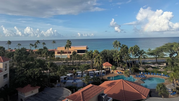 A resort with a swimming pool, palm trees, and a view of the ocean. - 2-bedroom Penthouse Condo in Divi Golf & Beach with breathtaking Oceanfront view (Oranjestad)