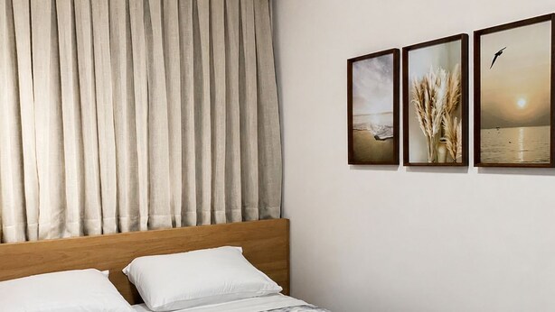 A hotel room with a bed, curtains, and three framed pictures on the wall.