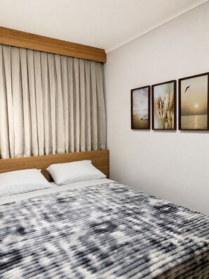 A hotel room with a bed, curtains, and three framed pictures on the wall.