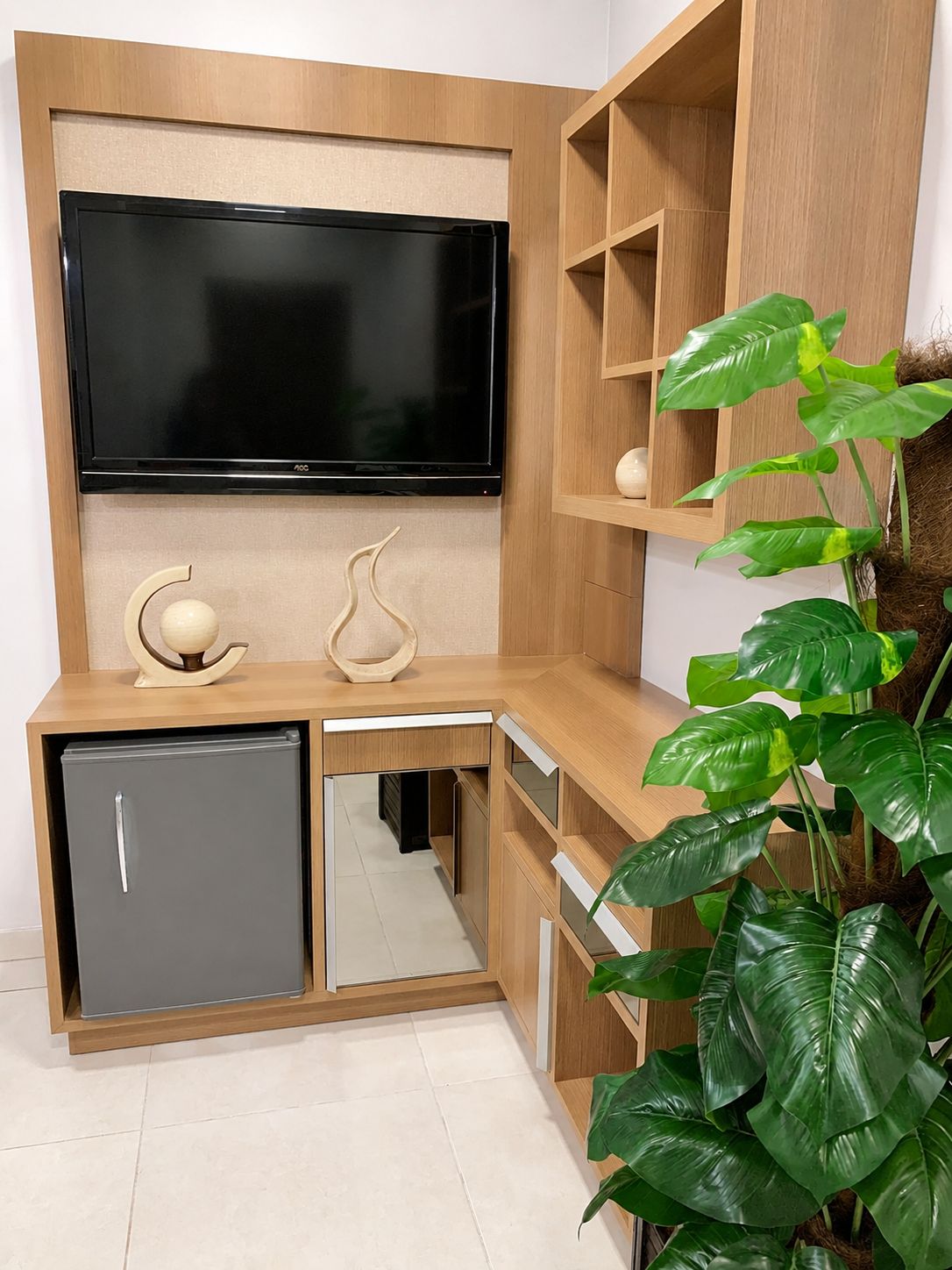 A compact living space with a built-in TV, a small refrigerator, and a plant.