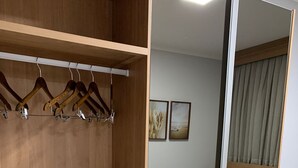A hotel room with a wooden wardrobe, a bed with a grey patterned duvet, and a large mirror reflecting the room.