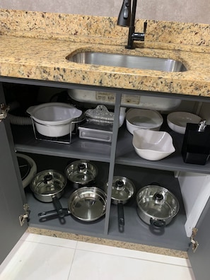 Een keuken met granieten aanrecht, een roestvrijstalen spoelbak en diverse keukengerei, waaronder pannen, braadpannen en een afdruiprek.