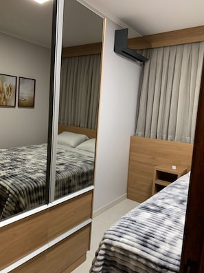 A bedroom with a bed, a bedside table, a mirror, and a window with curtains.