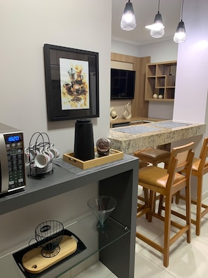 A modern kitchen with a coffee machine, a framed picture, and a dining area with chairs and a table.