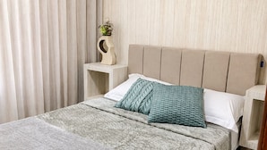 A bedroom with a bed, a nightstand, a wall-mounted shelf, and a curtain.