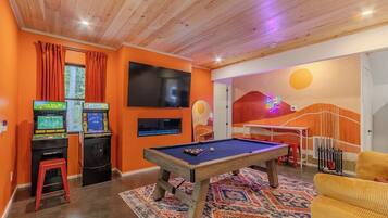 A room with a pool table, arcade games, and a TV.