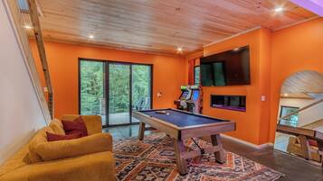 A room with a pool table, a sofa, a television mounted on the wall, and a staircase.