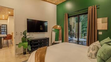 A bedroom with a large bed, a TV mounted on the wall, a dresser, and a window with curtains.