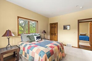 A bedroom with a large bed, two bedside lamps, a window with a view of trees, a door, and a mirror reflecting the room. - Browns & Bows Cabin on Missouri River (Cascade)