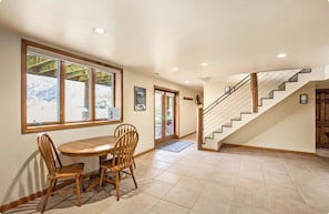 A dining area with a wooden table and chairs, a staircase, and a view of the outdoors.