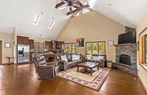 A spacious living area with a fireplace, leather furniture, and a kitchen in the background. - Browns & Bows Cabin on Missouri River (Cascade)