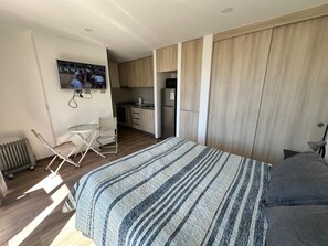 A bedroom with a bed, a desk, and a kitchenette in the background. - Espaço Bosque Pucón: Nature Near the City Center (Pucon)