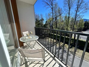 A balcony with a glass table and chairs, a wine glass, and a view of trees and a road. - Espaço Bosque Pucón: Nature Near the City Center (Pucon)