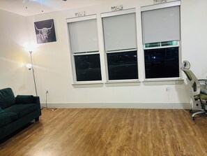 A room with a green sofa, a standing lamp, a framed artwork, and three windows with blinds. - Serene 1-bedroom apartment with luxurious living-Downtown Dallas (Dallas)