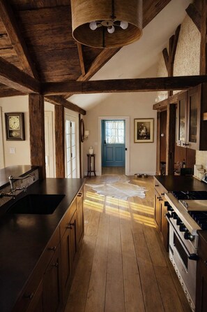 A kitchen with wooden beams, a central island, a stove, and a blue door. - Historic 1705 Farmhouse Near Thunder Ridge Ski Area, Sleeps 6 (Patterson)
