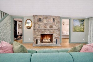 A living room with a stone fireplace, a green sofa, and a staircase leading to another room. - Historic 1705 Farmhouse Near Thunder Ridge Ski Area, Sleeps 6 (Patterson)