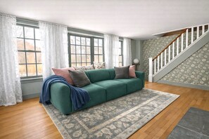A living room with a green sofa, patterned rug, and a staircase with floral wallpaper. - Historic 1705 Farmhouse Near Thunder Ridge Ski Area, Sleeps 6 (Patterson)
