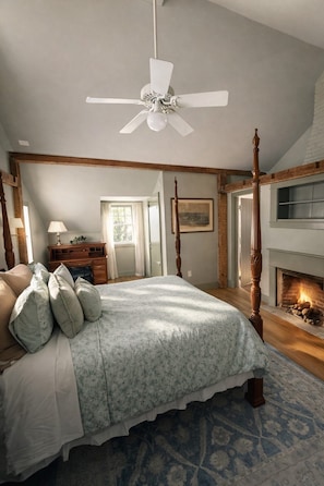 Une chambre à coucher avec un lit à baldaquin, un ventilateur de plafond, une cheminée et une vue sur l’extérieur.