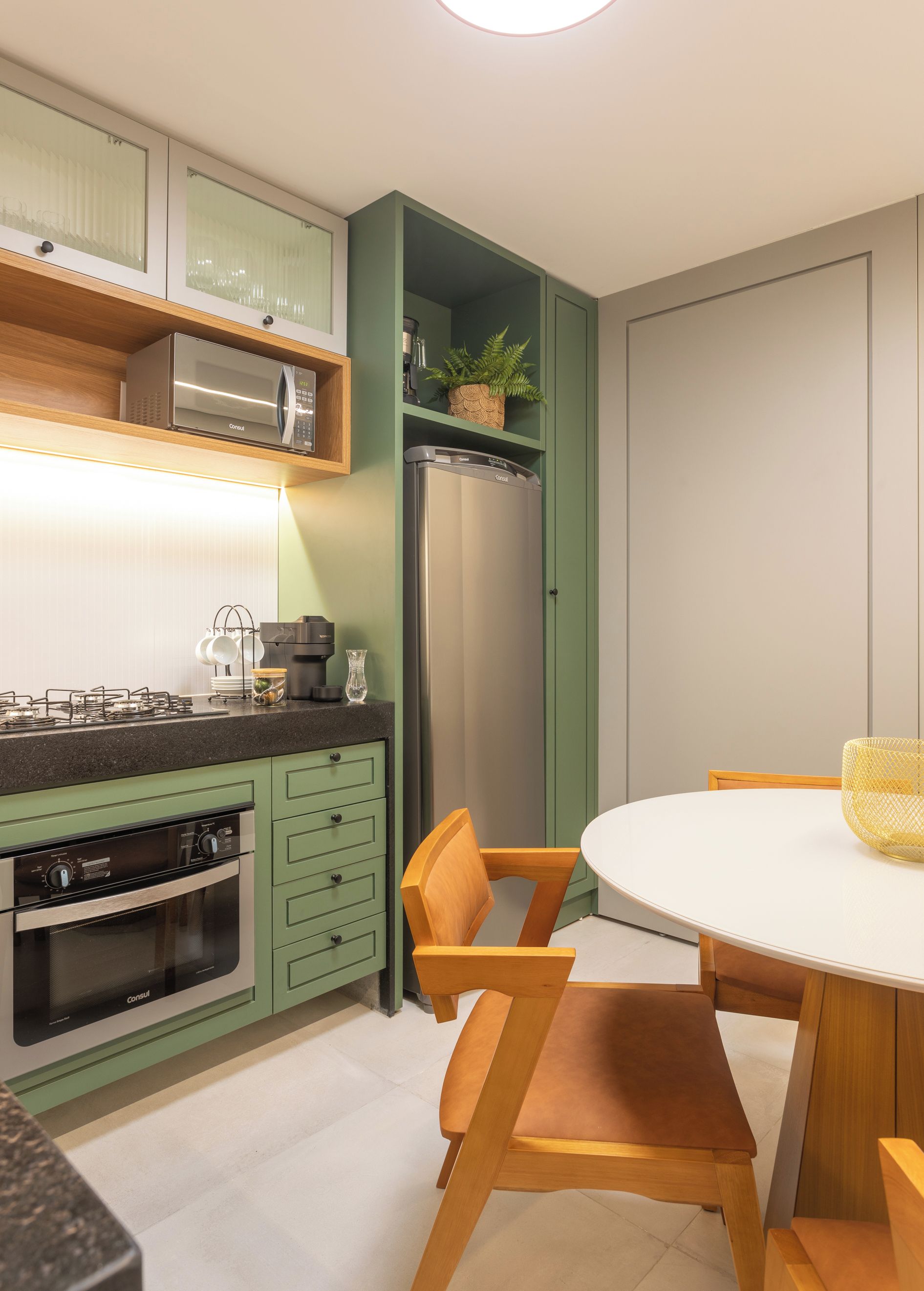 Cozinha moderna com armários verdes, geladeira de aço inoxidável e área de jantar com mesa branca e cadeiras de madeira.